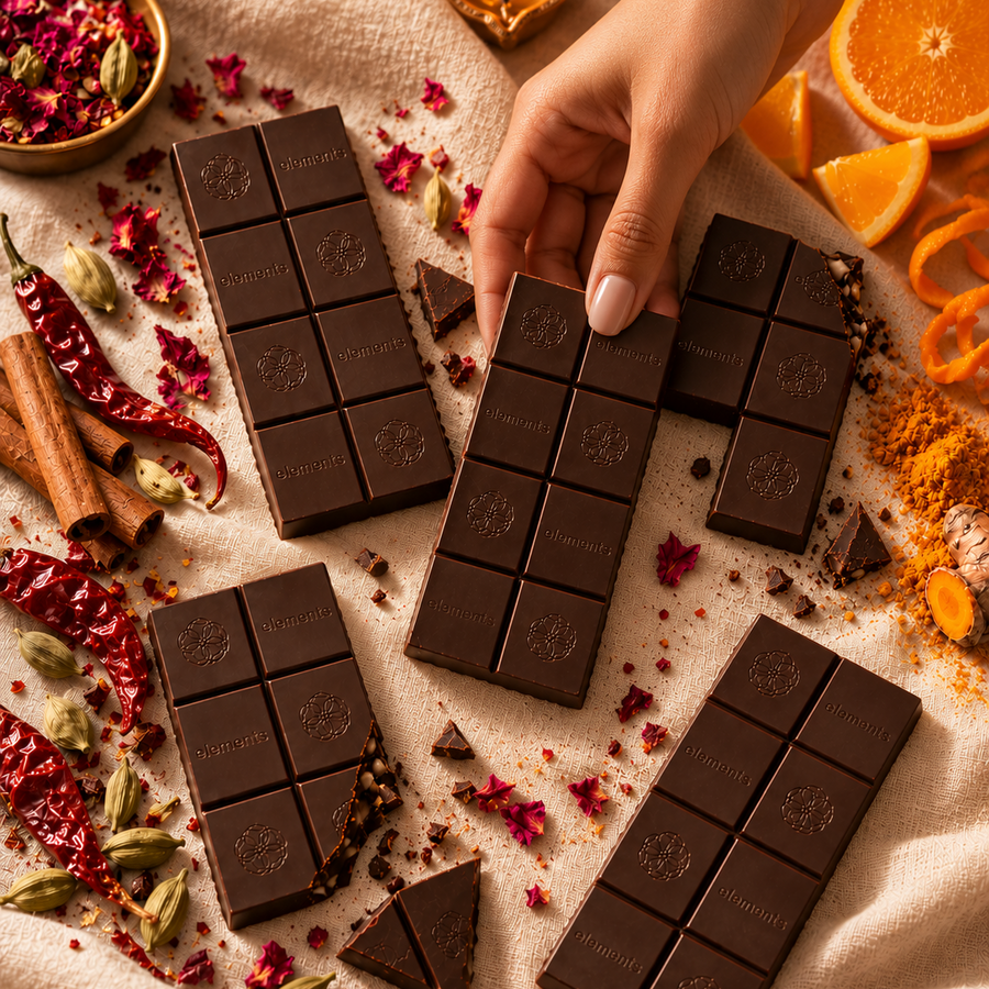 A hand picking up an Elements dark chocolate bar, with orange, chillies and spices around
